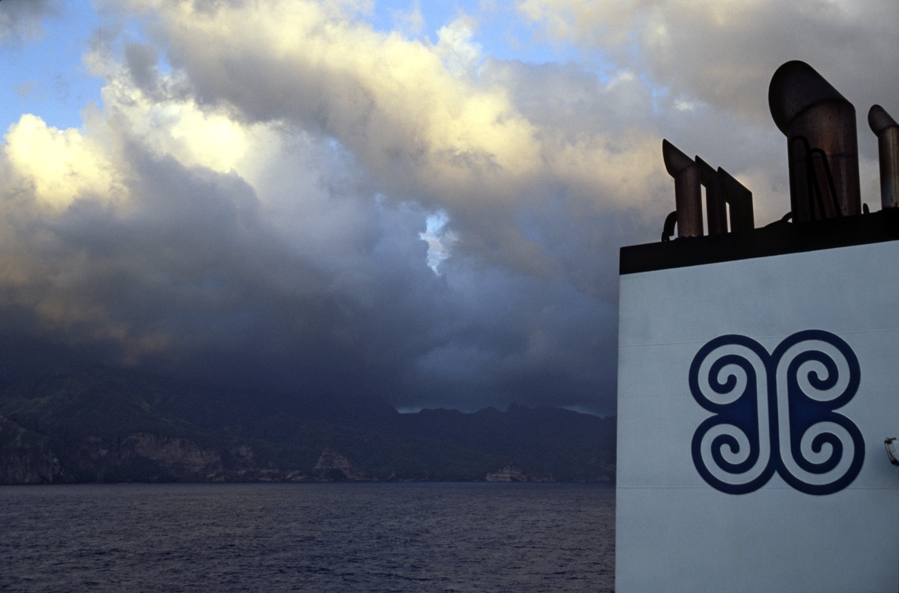 pol05_0725m.jpg - Iles Marquises, Ua Pou l'adieu aux îles Marquises : le soleil couchant sur la côte d'Ua Pou, et le logo de l'Aranui qui ressemble à la croix marquisienne